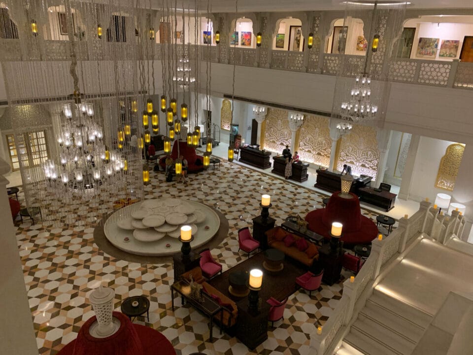 A fountain comprised of circles sits in the middle of a well lit lobby. Crimson velour seats and intricate lattice match the geometric tiles
